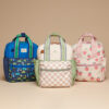 Three patterned backpacks are on display: the blue one has a dinosaur design, the beige one features a checkered pattern, and the pink one is adorned with strawberry prints.