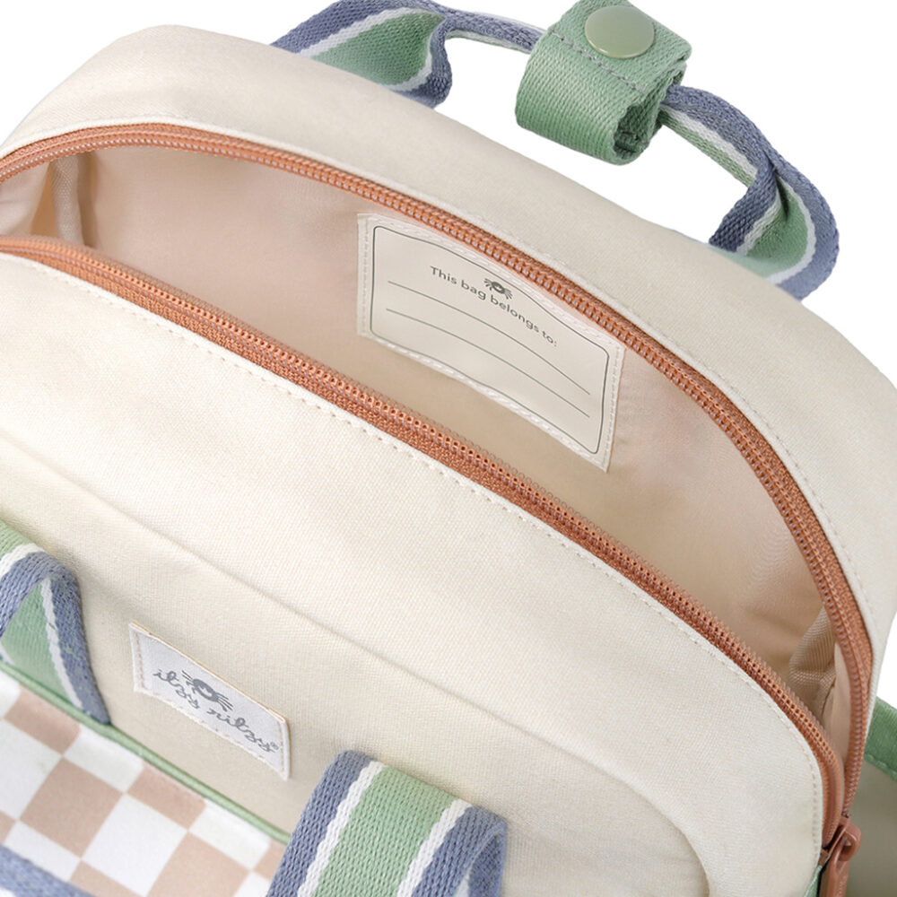 The Itzy Ritzy Sweetie Strap Plus Bear Silicone Pacifier Clip, featuring a cream-colored design with a beige zipper that's partially open to reveal an inner pocket labeled "This bag belongs to" with space for personalization. The handle and trim come with stylish green and blue accents.