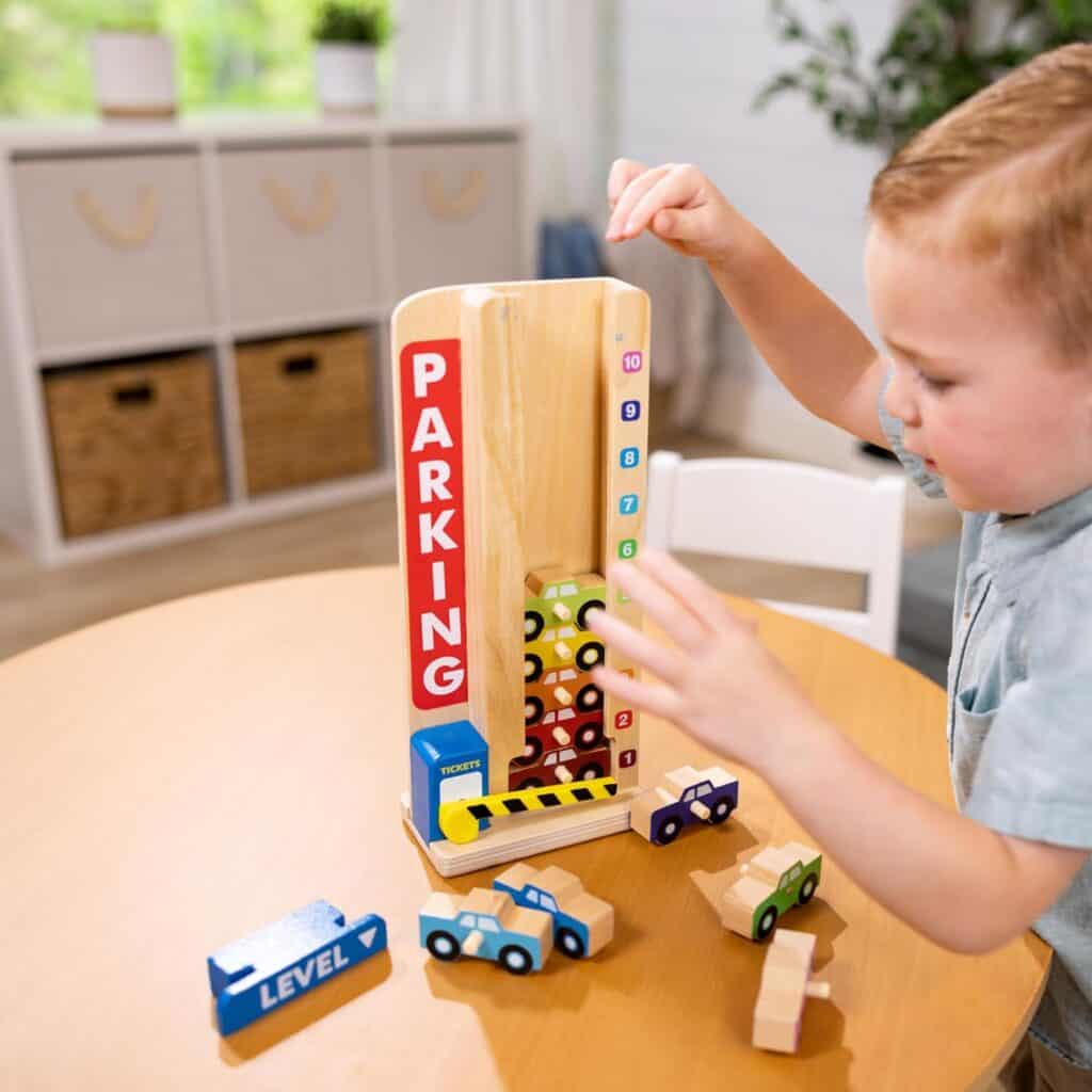 A young boy playing with a Melissa & Doug Stack & Count Wooden Parking Garage With 10 Cars at a table.