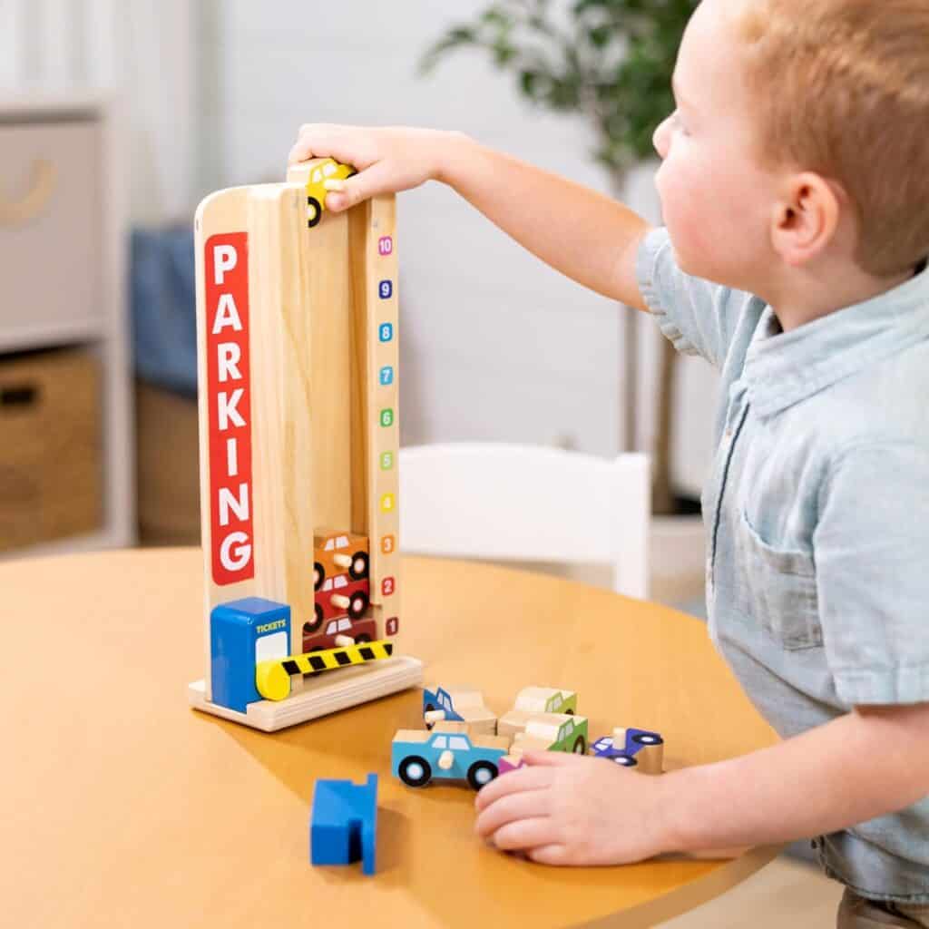 A young boy playing with a Melissa & Doug Stack & Count Wooden Parking Garage With 10 Cars at a table.