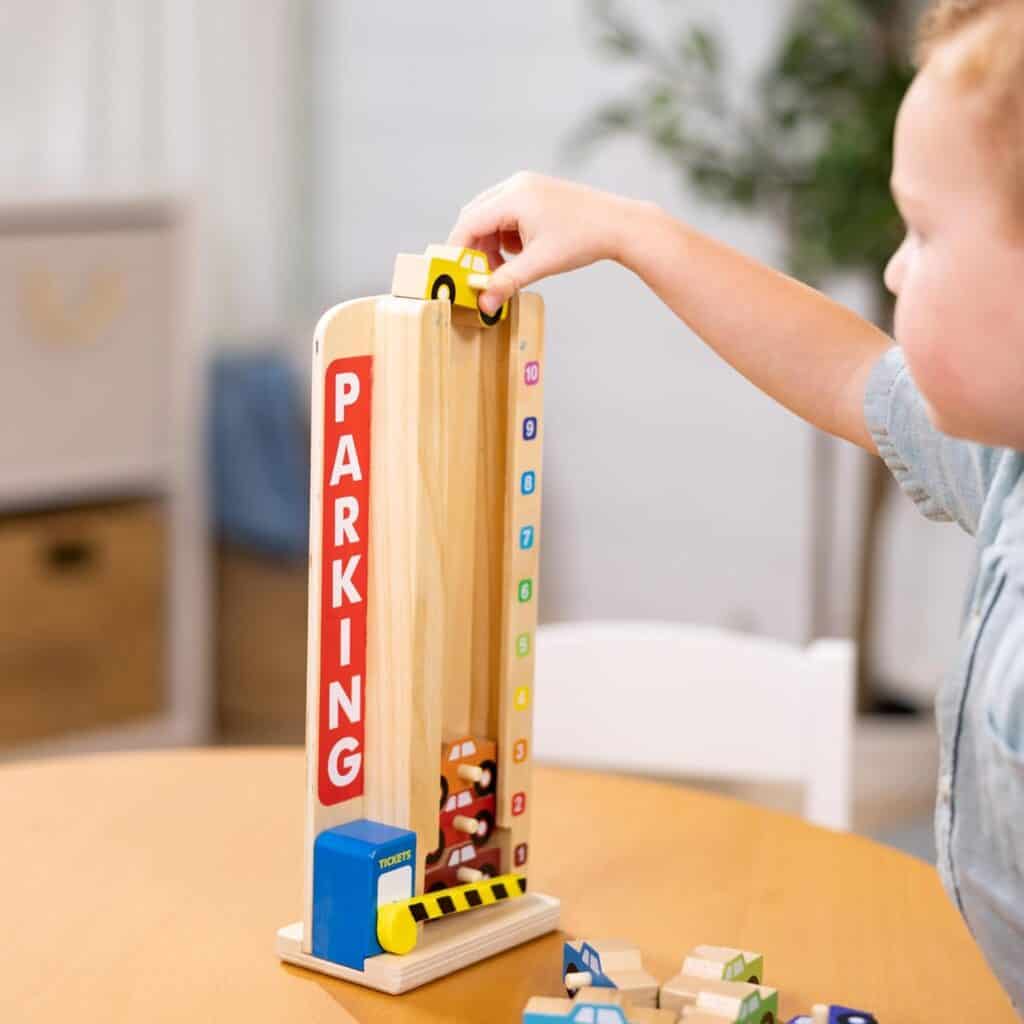 A child is playing with a Melissa & Doug Stack & Count Wooden Parking Garage With 10 Cars.