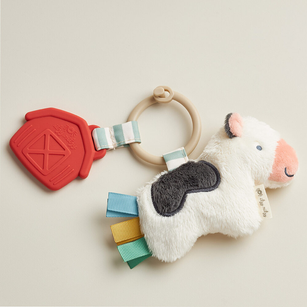 A baby toy featuring a plush cow with multicolored ribbons and a red barn-shaped teether attached to a ring.