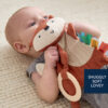 An infant lying on a soft surface holding a plush fox toy labeled "SNUGGLY SOFT LOVEY.