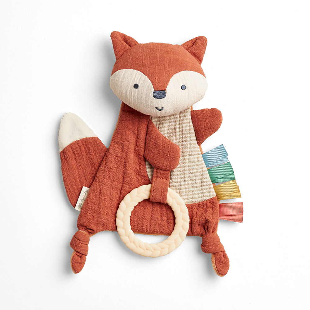 Brown and beige fox-shaped stuffed toy with a textured body, holding a rubber teething ring, and colorful fabric tags on its side.