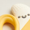 Close-up of the Itzy Ritzy Chew Crew Silicone Teether with Handles, designed as a smiling banana in yellow and white, featuring a textured peel and a soft design for chewing.