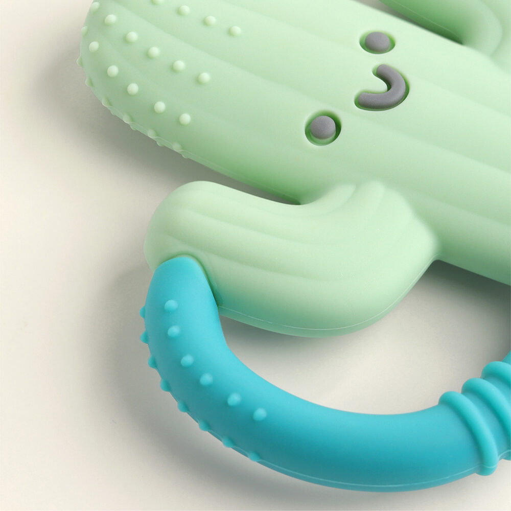 The Itzy Ritzy Chew Crew Silicone Teether with Handles, featuring a green cactus shape with a smiling face and a blue handle, is shown on a plain background.