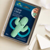 A packaged cactus-shaped silicone teether labeled "Itzy Ritzy Chew Crew Silicone Teether with Handles" for ages 3 months and up. The package is open in a box with an envelope and ribbon nearby.