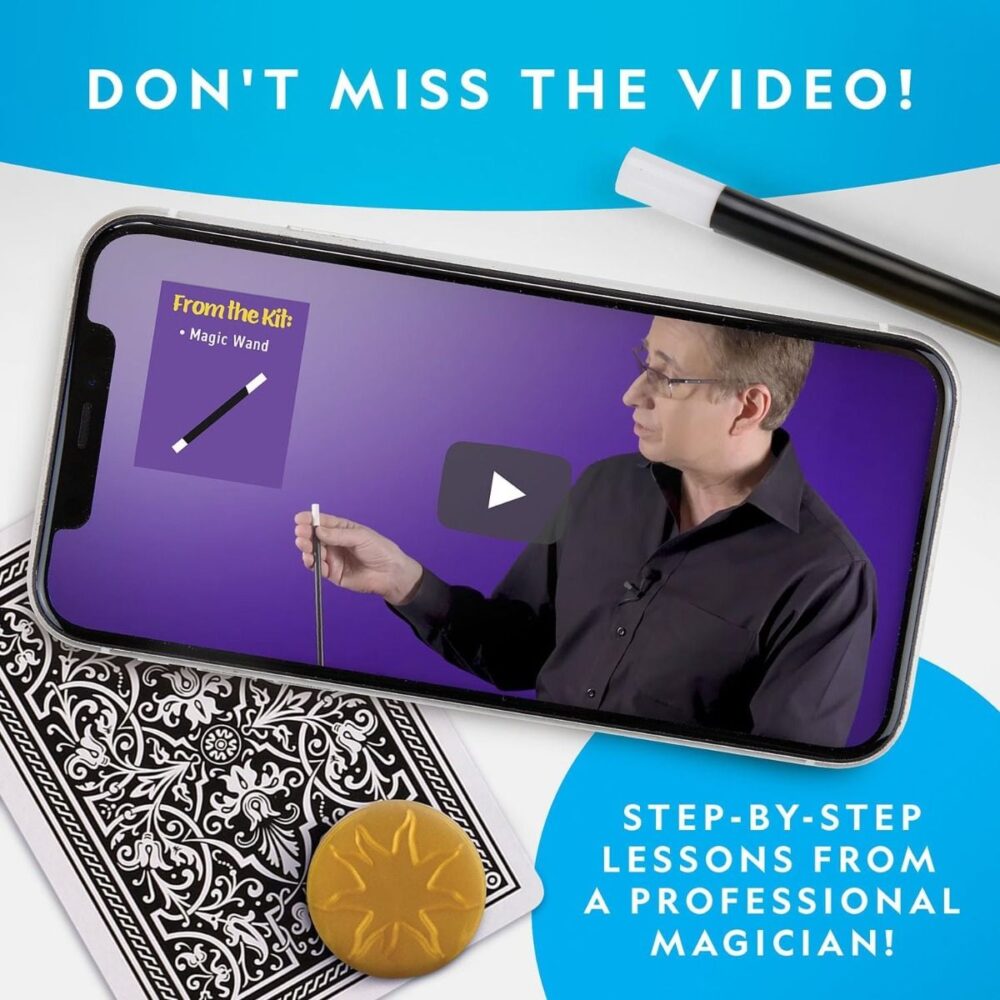 Smartphone displaying a video tutorial by a magician on a purple background, a text reading "From the Kit: National Geographic Magic Set 5 Tricks Perform Magic Kit Wand Card Cup Balls STEM Educational NatGeo NGEO" visible. Nearby are a deck of cards, a wand, and a gold coin. Text: "STEP-BY-STEP LESSONS FROM A PROFESSIONAL MAGICIAN!.