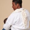 A person in a white shirt and jeans sits on a stool, with their back facing the camera, using the Breastfeeding Boss—a multitasking must-have for nursing, swaddling, and more—to cradle a baby.