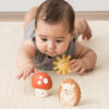 Baby lying on stomach reaching for the Itzy Ritzy Sensory Blocks 10-Piece Set with a plush sun and hedgehog nearby on a carpeted floor.