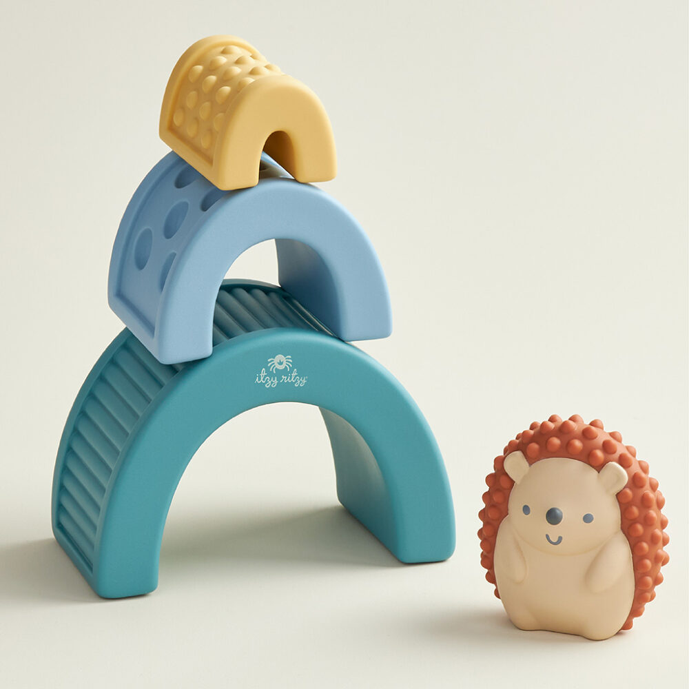 A colorful stack of Itzy Ritzy Sensory Blocks 10-Piece Set featuring a blue arch and a yellow piece on top, accompanied by a smiling hedgehog-shaped toy, on a neutral background.