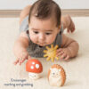 Infant lying on stomach on a carpet, reaching towards an Itzy Ritzy Sensory Blocks 10-Piece Set and a toy hedgehog.