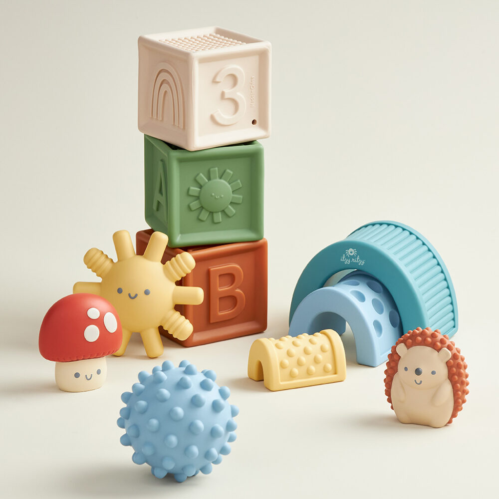 A collection of Itzy Ritzy Sensory Blocks 10-Piece Set including stackable blocks, a textured ball, and whimsical animal-shaped toys on a light background.