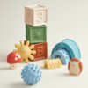 A collection of Itzy Ritzy Sensory Blocks 10-Piece Set including stackable blocks, a textured ball, and whimsical animal-shaped toys on a light background.