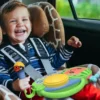 A child sits in a car seat laughing and holding the Cocomelon Toy My First Sing Along Boombox with a working microphone and buttons, surrounded by a giraffe-patterned cushion.