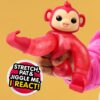 Hand holding a red stretchable toy monkey with a happy face. Text on the image reads, "Stretch, pat, and jiggle me, I react!.