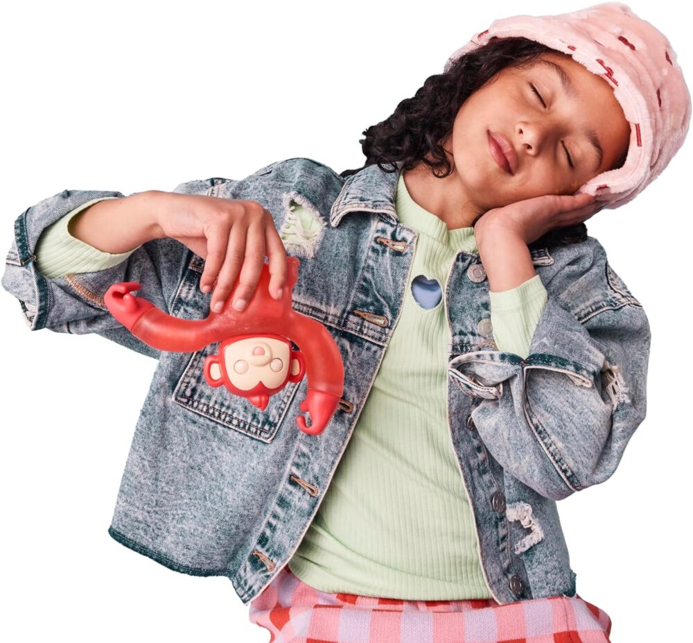 A young girl wearing a bucket hat and denim jacket holds a red toy monkey while resting her head on her hand.