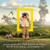 A child in safari clothing looks through binoculars in a prehistoric-themed landscape with dinosaurs, mountains, and a volcano. The National Geographic logo is in the background with text beneath: "National Geographic Break Open 10 Premium Geodes.