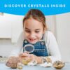 A young girl examines rock geodes with a magnifying glass on a table. The text at the top reads "DISCOVER CRYSTALS INSIDE." Several open geodes revealing crystals are spread out in front of her. National Geographic Break Open 10 Premium Geodes