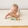 Baby lying on a rug playing with a wooden rainbow toy.