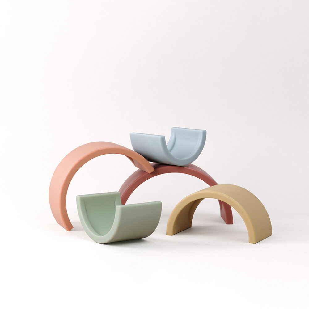 Pastel-colored arch toys nested together, with two forming a circle and one additional arch supporting two bowl-like pieces on a plain background.