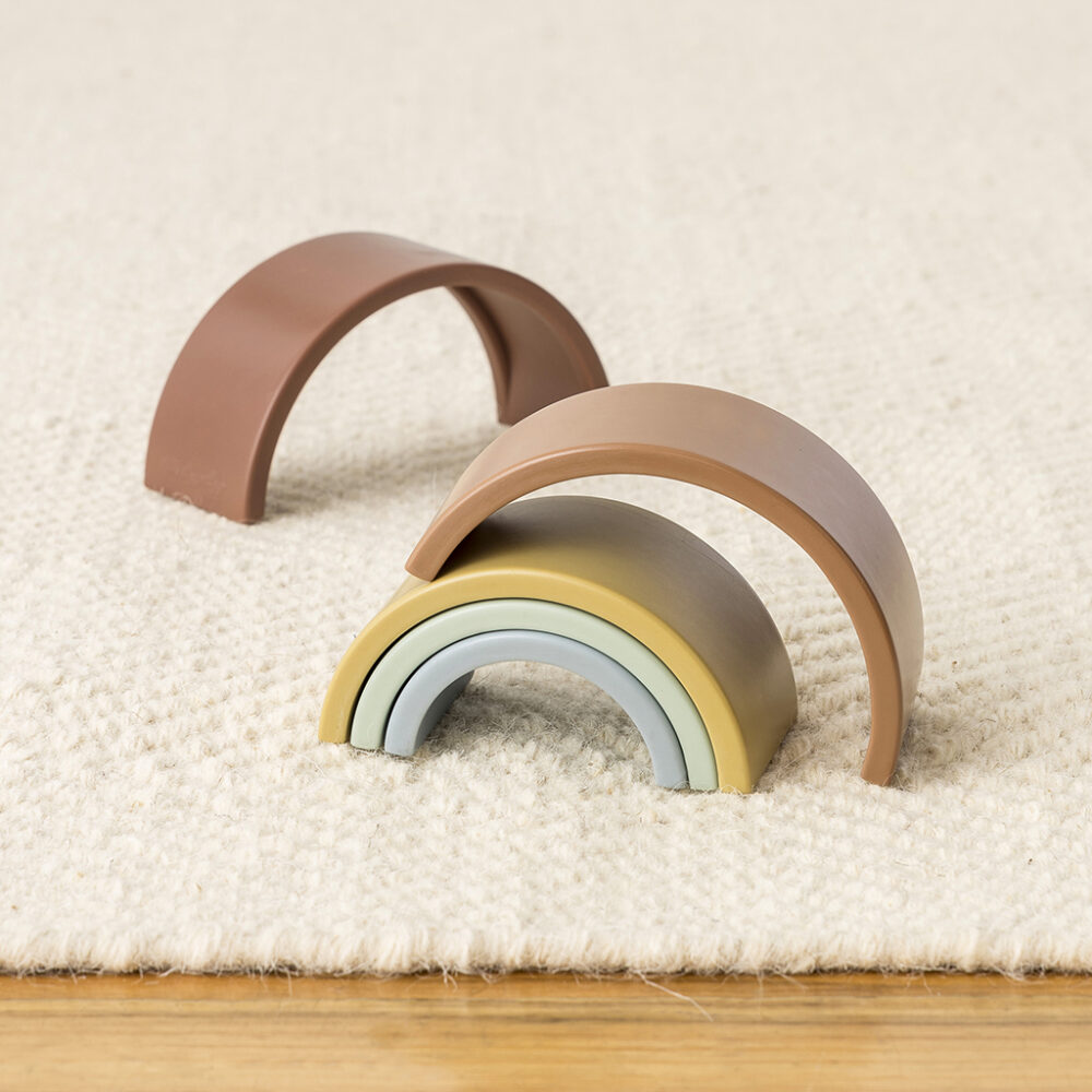 Wooden rainbow toy pieces in pastel colors, stacked in an arch shape on a cream carpet.