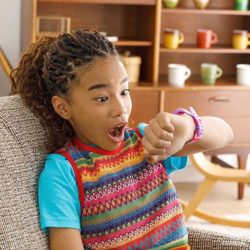 A young child with braided hair looks surprised while glancing at their wrist, which has a colorful watch. The child is indoors, sitting in a living room with shelves and colorful mugs in the background.