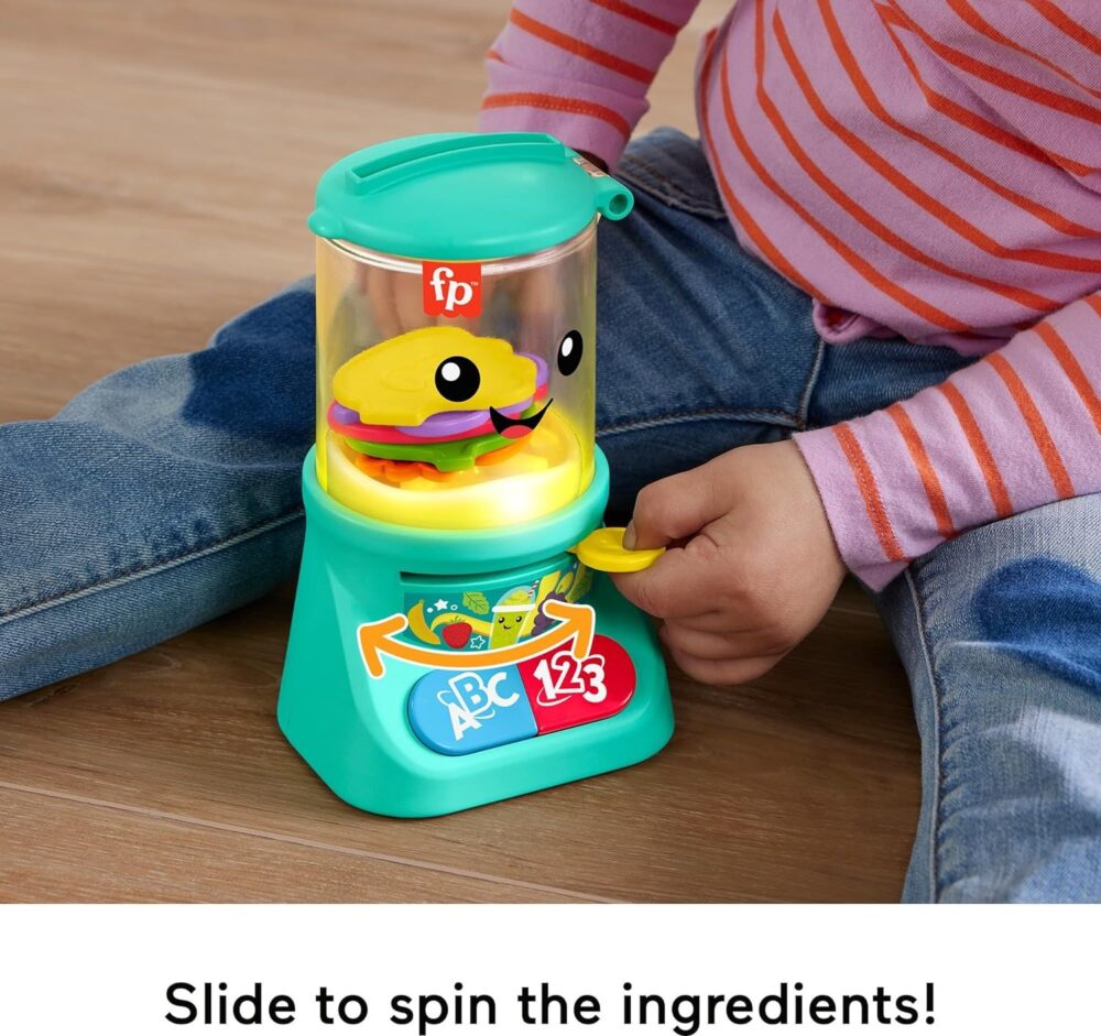 A child is playing with a Fisher-Price Laugh & Learn Baby & Toddler Toy Counting & Colors. The toy has a transparent top, a smiling face graphic, and labeled buttons on the front. The child is wearing blue jeans and a red-striped shirt.