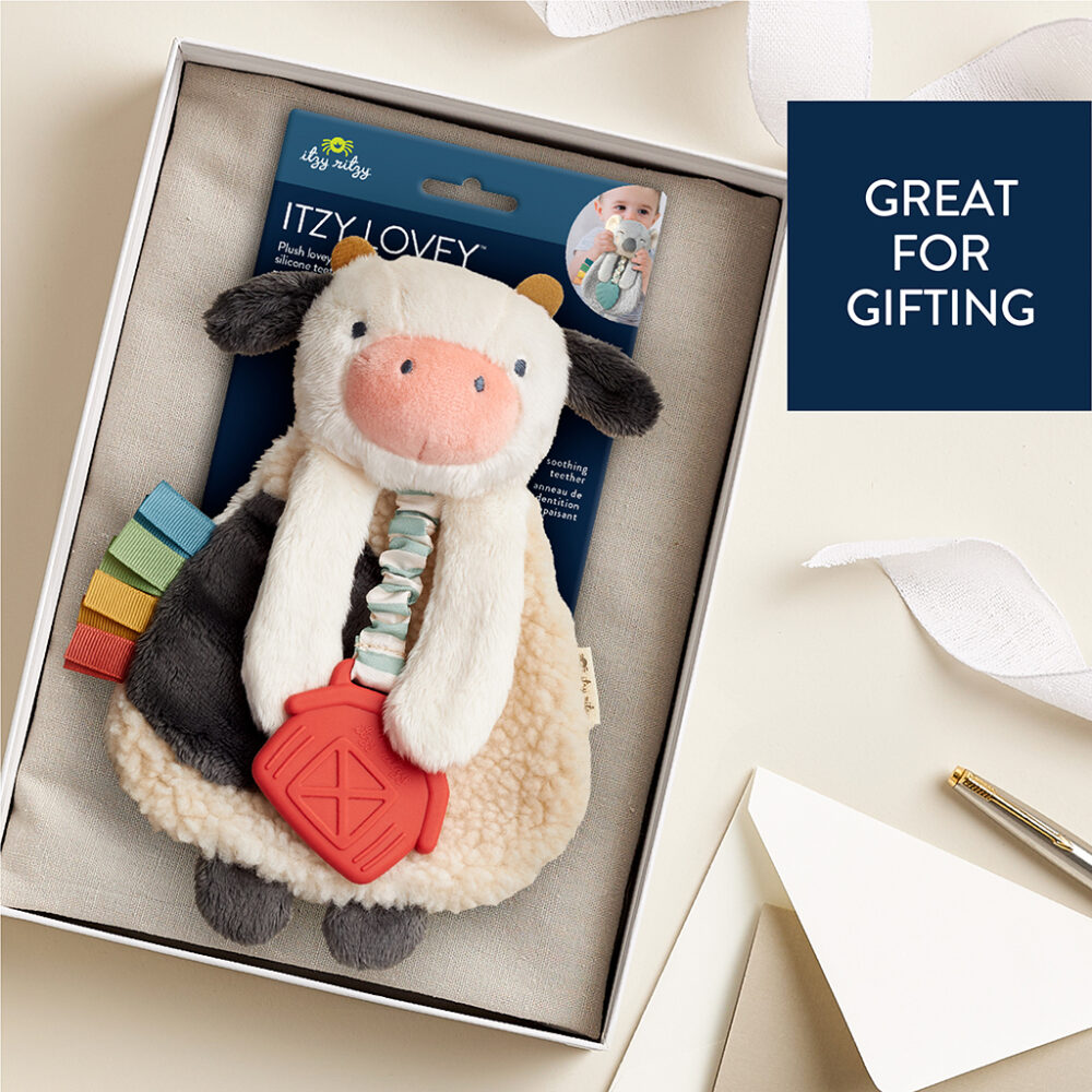 A boxed cow-themed baby plush toy with a red barn-shaped teether and a note saying "Great For Gifting" beside it.