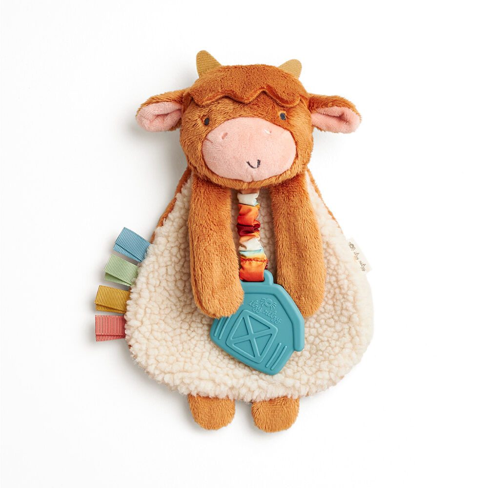 Plush toy shaped like a cow with a soft beige body, brown head, and ears. Attached to it is a blue teething toy and colorful fabric tabs on one side. Ideal for infants and toddlers.