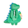 A green plush dinosaur toy with a textured belly, blue spikes along its back, and colorful fabric tags on its side. The toy has a small floral-patterned bow tie.