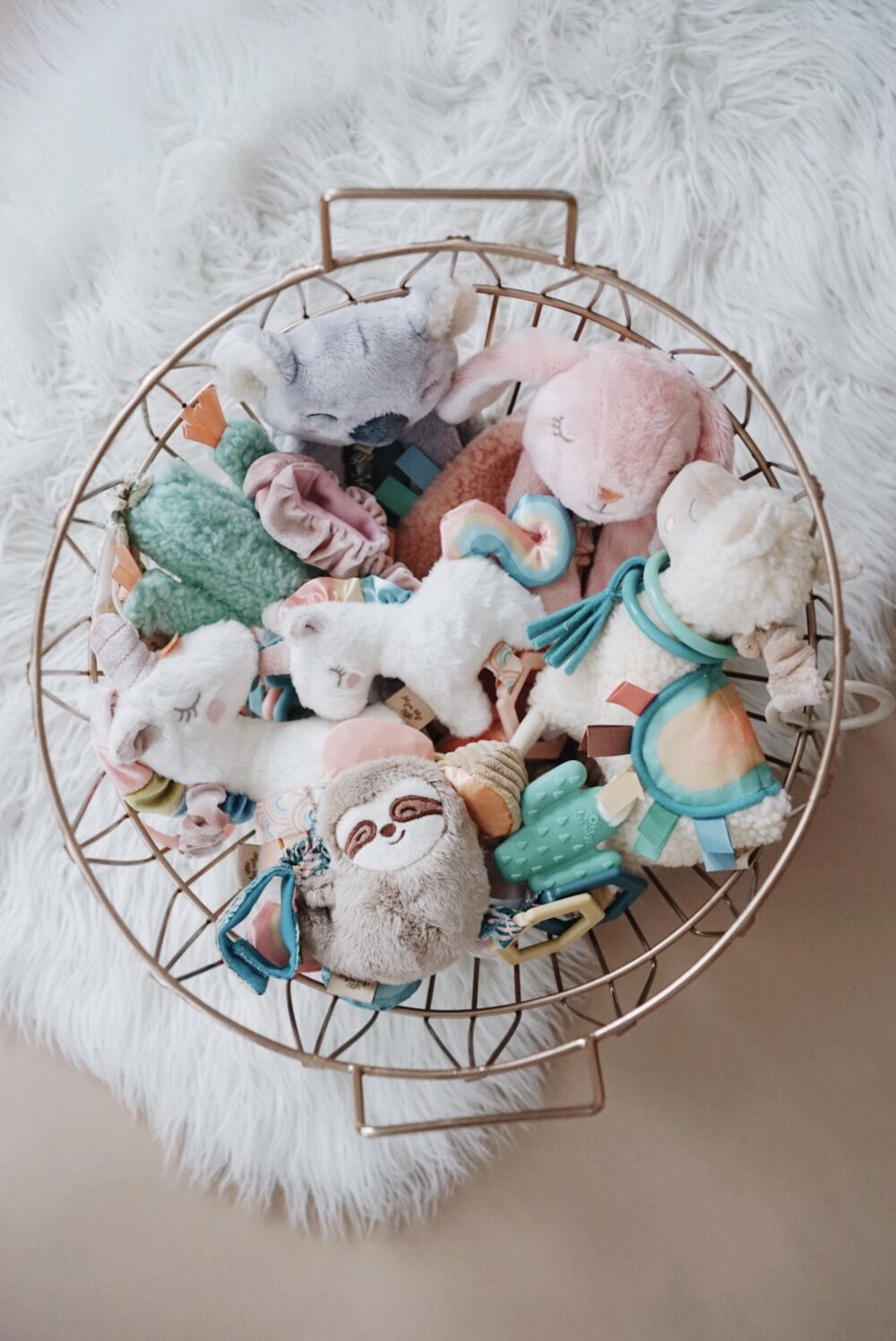 A round wire basket filled with various plush toys, including animals and characters, placed on a fluffy white surface.