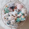 A round wire basket filled with various plush toys, including animals and characters, placed on a fluffy white surface.