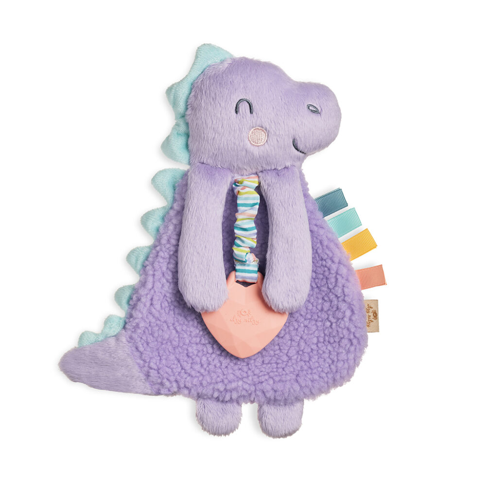 Plush purple dinosaur toy with a soft blue spine, holding a rubber heart-shaped teething ring. It has various colorful fabric tags attached to its body.