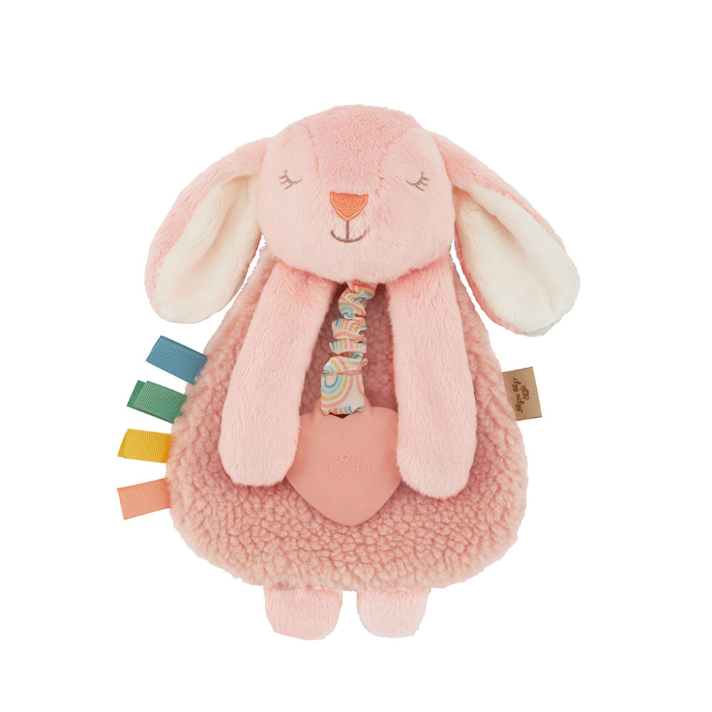 A soft, pink plush bunny toy with long ears and various colorful fabric tags attached to its side, holding a heart-shaped accessory.