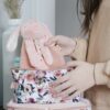 A person is placing a pink stuffed rabbit toy into a floral-patterned bag. Two stacked bags are visible. The background includes a white vase with dried plants.