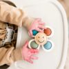 Baby hands playing with an Itzy Pop & Whirl - Fidget Spinner Highchair, Travel & Bath Toy on a high chair.