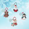 Four Itzy Ritzy - Itzy Pal - Plush Pal Infant Toy with Silicone Teether keychains shaped like santa claus, a bear, a penguin, and a deer against a snowy background with snowflakes.