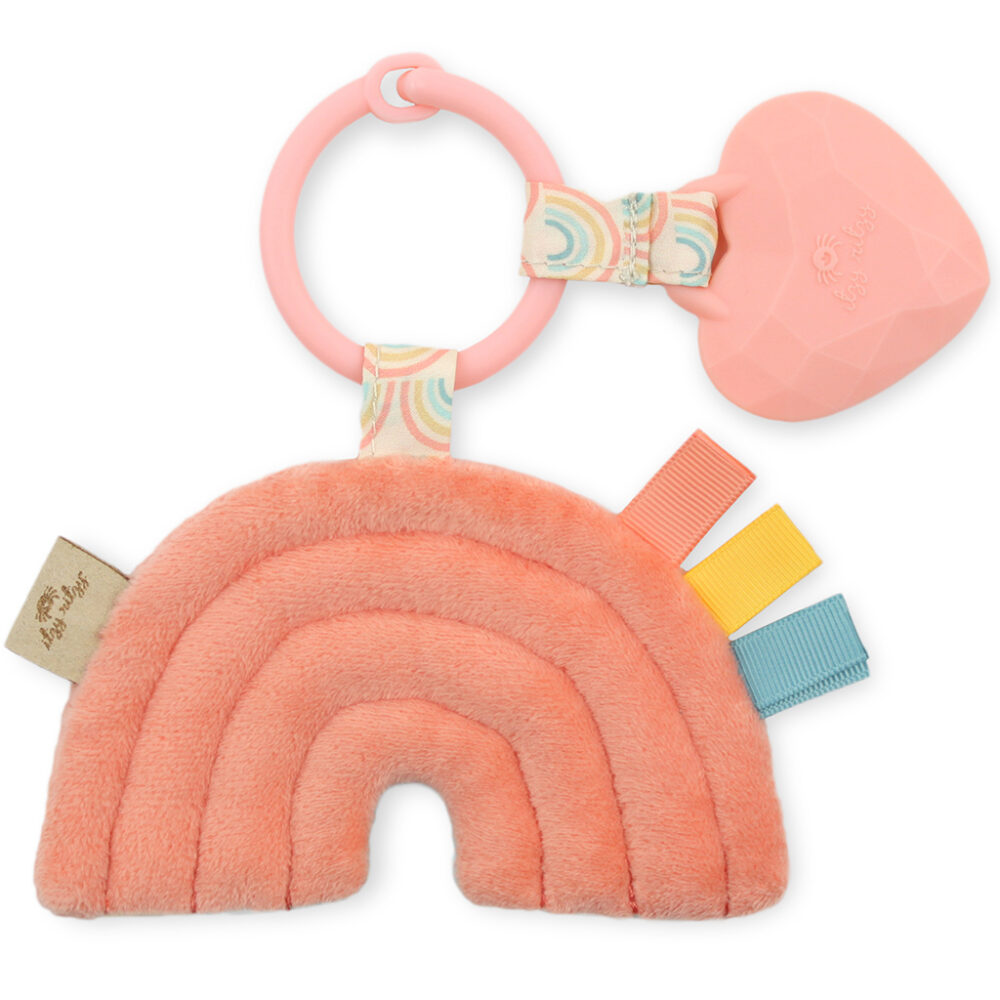 A pink Itzy Ritzy - Itzy Pal plush baby toy shaped like a rainbow with a teething ring and various textured tags attached.